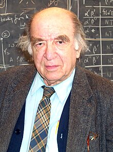 chest high portrait in suit and tie with longish hair in front of blackboard calculations