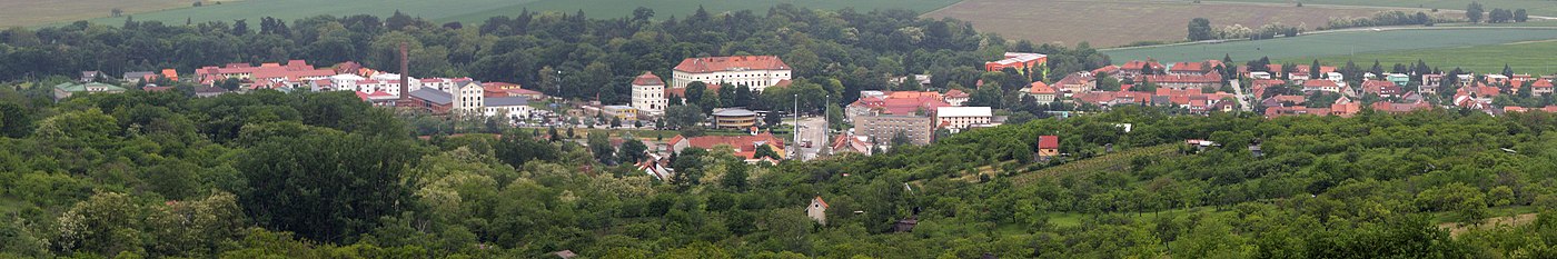 Panoramo de Židlochovice el belvedero Akátová věž. Meze kastelo kun parko, maldekstre fumtubo kaj konstruaĵoj de eksa sukerfarejo.