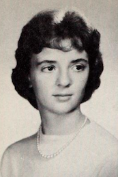 A young white woman with dark hair in a set style, wearing a light-colored crewneck top and a strand of pearls