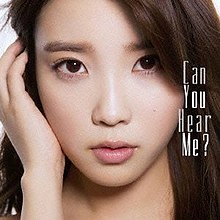 A close-up of the face of a woman with long brown hair. She holds her right hand up to her right ear. To the right of the photo are the words "Can You Hear Me" in white capital letters.