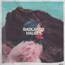 Halsey wears a pink fur coat and blue hair in front of a large rock. The words "BADLANDS – HALSEY" cover her face.