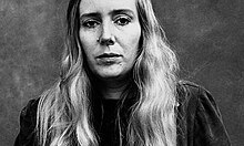 Black and white portrait photograph of Lorna Sage. She is dressed casually, has long hair and is looking directly into the camera