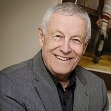 Late-middle-aged man with light grey hair, wearing a dark grey striped suit jacket