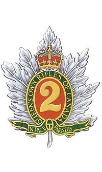 Image en couleur d'un insigne militaire composé d'une feuille d'érable d'argent avec, au centre, le chiffre « 2 » d'or sur fond rouge entouré d'un listel de forme ovale vert liséré d'or portant l'inscription « Queen's Own Rifles of Canada » en lettres majuscules d'or surmonté d'une couronne royale au naturel ainsi que, brochant sur la tige de la feuille d'érable, un listel vert liséré d'or portant l'inscription « In Pace Paratus » en lettre majuscules d'or