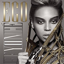 The front face of Beyoncé, in greyscale. She is wearing heavy make-up and has her hair folded back. A metallic cape is wound around her neck, which she holds at her front. Her right hand is empty, but on her left hand she wears a metallic glove. On the right of the image, the words "Ego" and "Beyoncé" are written in capital fonts. The word Ego and Knowles' cape is colored gold.